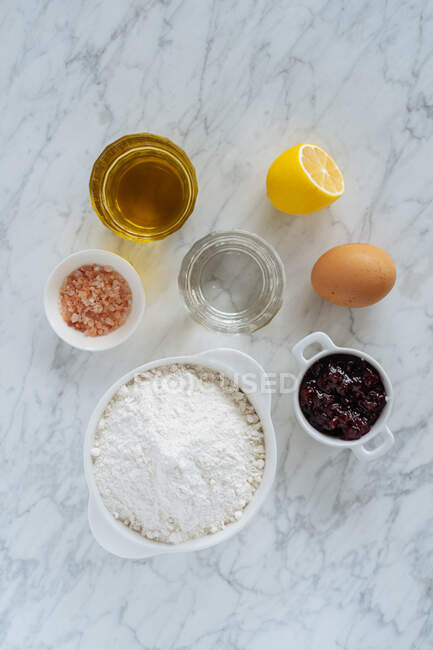 Vista dall'alto della serie di ingredienti per la ricetta di cottura tra cui farina bianca e uova e bicchieri con prodotti liquidi con limone e sale su sfondo di marmo — Foto stock