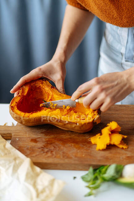 Mulher de colheita com faca de cozinha preparando metade da abóbora de manteiga assada para enchimento em tábua de corte de madeira na mesa da cozinha — Fotografia de Stock