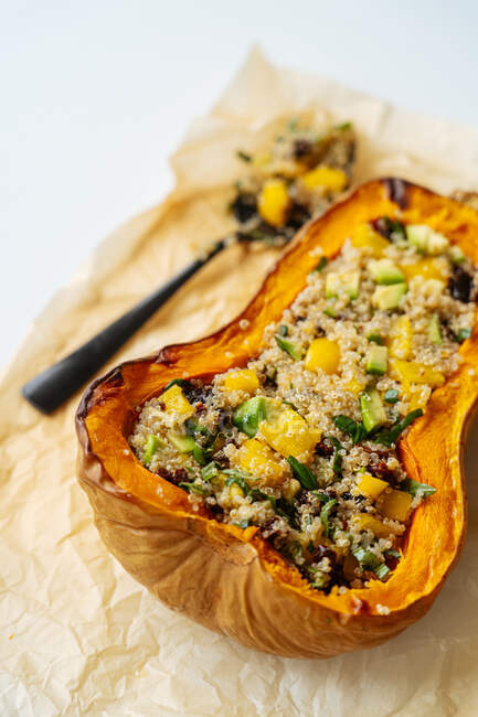 Closeup of appetizing tasty healthy baked stuffed butternut pumpkin with quinoa and vegetables placed on crumpled baking paper with spoon — Stock Photo