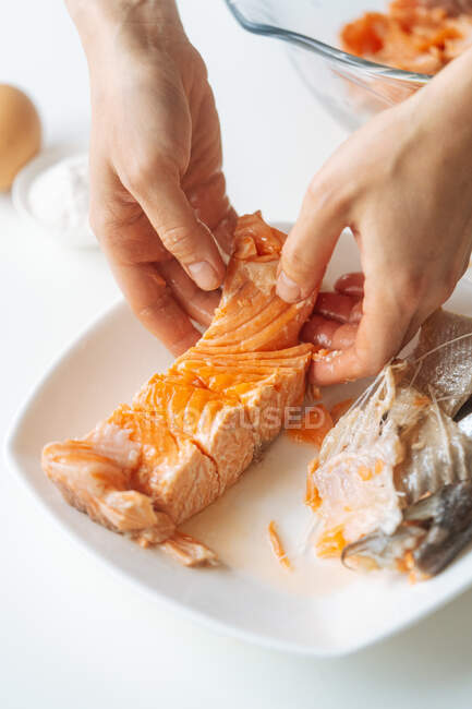 Mãos de corte de fêmea separando pedaço de salmão cozido de ossos enquanto prepara o jantar em casa — Fotografia de Stock