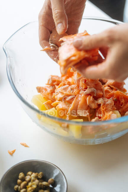 Crop hands of female putting pieces of cooked salmon fillet into transparent glass bowl with cut potatoes — Stock Photo