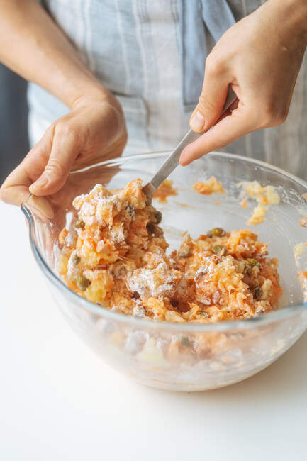 Coltivare le mani di femmina con cucchiaio mescolando ingredienti tritati in una ciotola di vetro trasparente durante la preparazione di ripieno in cucina di casa — Foto stock