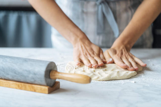 De dessus la culture cuire intensément pétrir la pâte avec les doigts sur la table de marbre avec rouleau à pâtisserie dans la cuisine — Photo de stock
