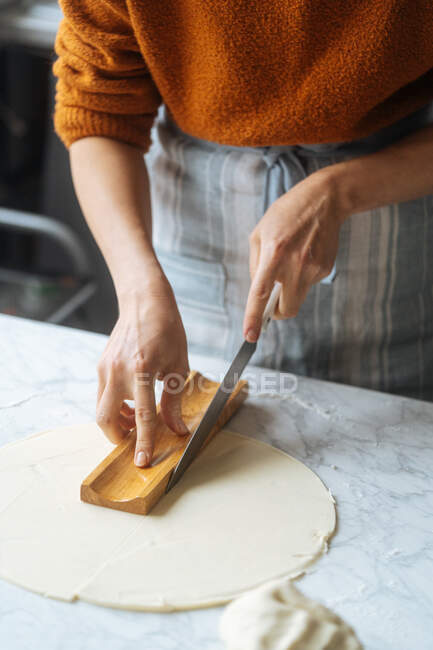 De dessus la culture cuisinier qualifié dans la pâte à découper tablier avec couteau en utilisant la forme sur la table dans la cuisine — Photo de stock