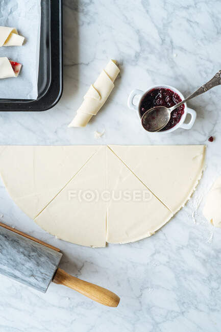 D'en haut morceau tranché cru de confiture de pâte et rouleau à pâtisserie sur table en marbre dans la cuisine — Photo de stock