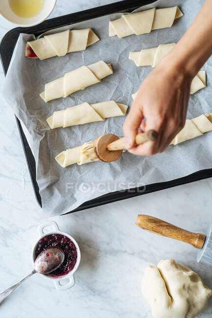 Von oben ernten qualifizierte Köchin sorgfältig Bürsten leckere Croissants auf Backblech auf dem Tisch in der Küche — Stockfoto