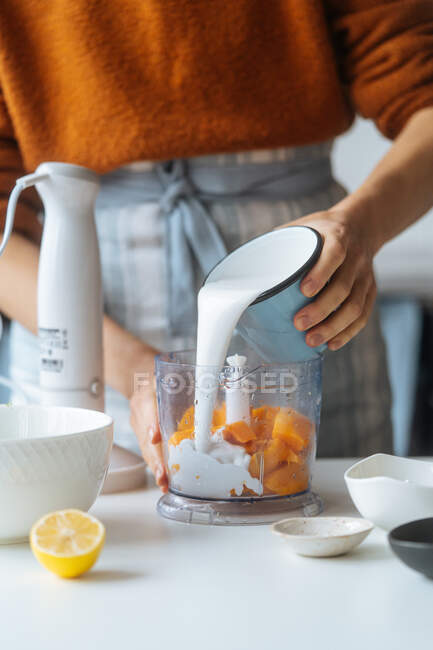 Ernteköchin gießt sorgfältig Milch in Mixer mit Kürbis Hand Tisch mit Zitrusfrüchten in leichter Küche — Stockfoto