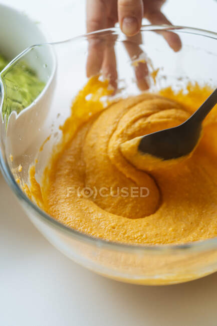 From above glass bowl with orange vegetable mixture in hands of crop cook stirring puree with spoon at table — Stock Photo