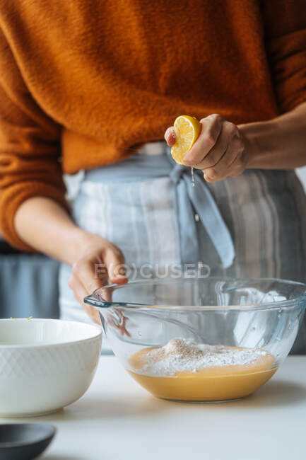 Glass bowl with orange vegetable mixture in hands of crop cook squeezing ripe lemon into puree at table — Stock Photo