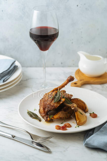 Köstliche, appetitlich gebratene Wachteln garniert mit Birnen und Blättern, serviert mit einem Glas Rotwein auf hellem Marmortisch — Stockfoto