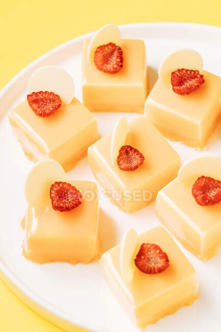 Closeup pieces of scrumptious pastry decorated with halves of fresh raspberries and white chocolate and placed on plate on yellow background — Stock Photo