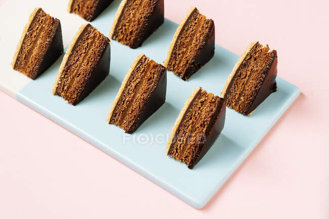 Von oben Stücke leckerer Schokoladenkuchen in Reihen auf blauem Brett auf rosa Hintergrund platziert — Stockfoto