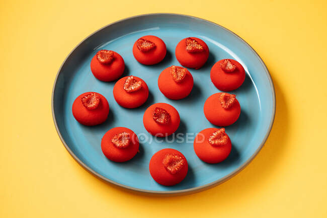 De arriba galletas en forma de bola roja con frambuesas frescas colocadas en el plato sobre fondo amarillo - foto de stock