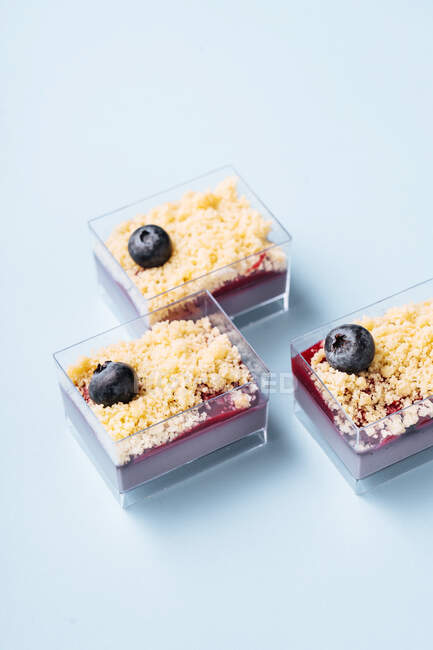 Dall'alto contenitori di vetro con porzioni di delizioso dessert ai mirtilli disposti su sfondo blu — Foto stock
