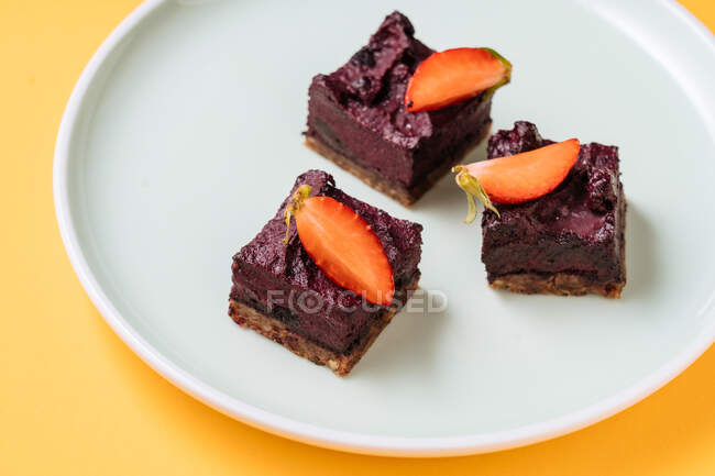 Pedaços de close-up de delicioso bolo de chocolate decorado com fatias de morangos frescos e colocado na placa no fundo amarelo — Fotografia de Stock