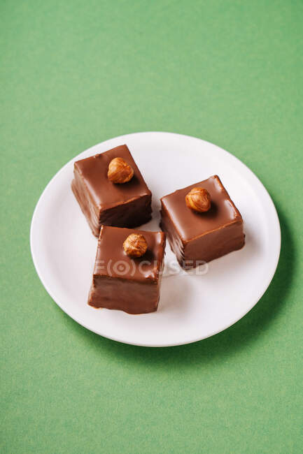 From above pieces of yummy pastry with chocolate icing and hazelnuts placed on plate on green background — Stock Photo
