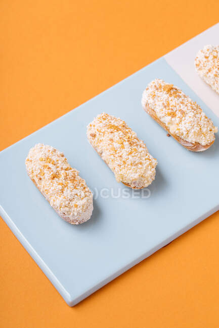 Von oben leckere weiche Eclairs mit weißem cremigem Zuckerguss in einer Reihe auf Bord vor orangefarbenem Hintergrund platziert — Stockfoto