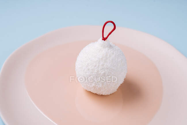 Closeup edible bauble with coconut icing placed on plate on blue background during Christmas celebration — Stock Photo