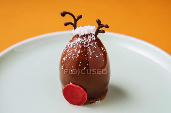 Closeup deer head shaped dessert for Christmas celebration placed on plate against orange background — Stock Photo