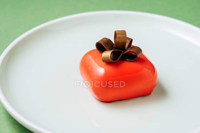 Крупним планом подарунковий десерт у формі з червоним глазур'ю та шоколадним бантом, розміщеним на тарілці на зеленому фоні — стокове фото