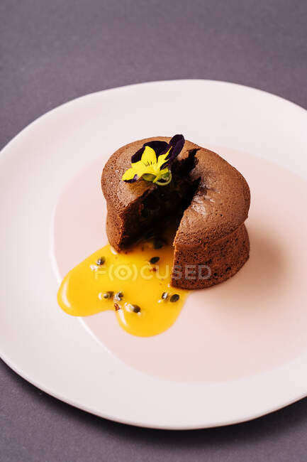 Сверху нарезанный шоколадный кекс с жидкой фруктовой начинкой и небольшим цветком, помещенным на тарелку — стоковое фото