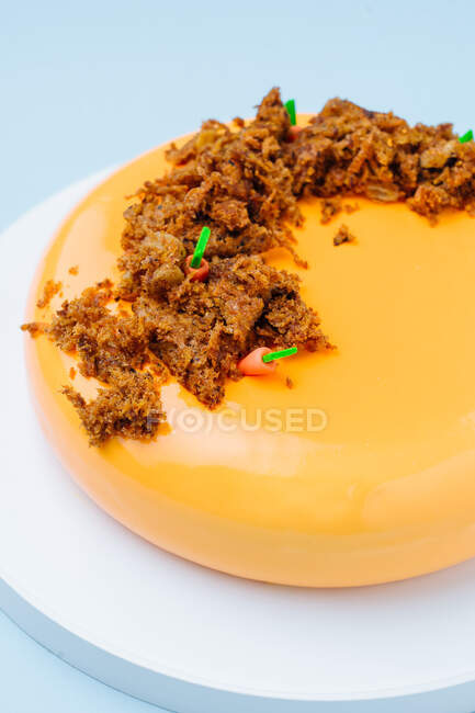 Von oben köstlicher Kuchen mit orangefarbenem Zuckerguss verziert mit süßer künstlicher Erde und kleinen Karotten auf blauem Hintergrund — Stockfoto
