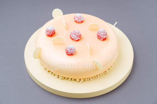 De arriba delicioso pastel con frambuesas frescas y glaseado de chocolate blanco colocado en la tabla redonda sobre fondo gris - foto de stock