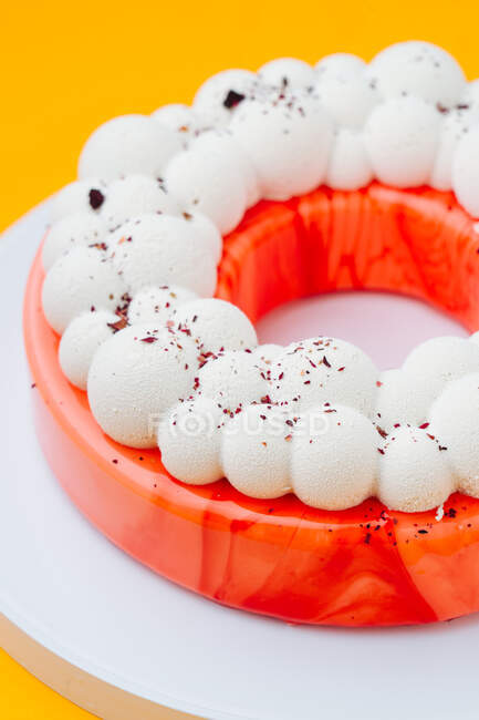 Dall'alto deliziosa torta a forma di anello con glassa di frutta rossa e bolle sulla parte superiore posizionata sul piatto sullo sfondo arancione — Foto stock
