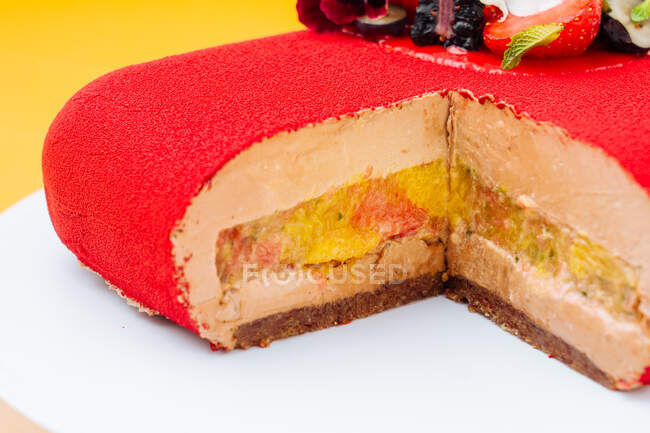 Primer plano sabroso pastel cortado con relleno de fruta dulce y glaseado rojo colocado en el plato - foto de stock