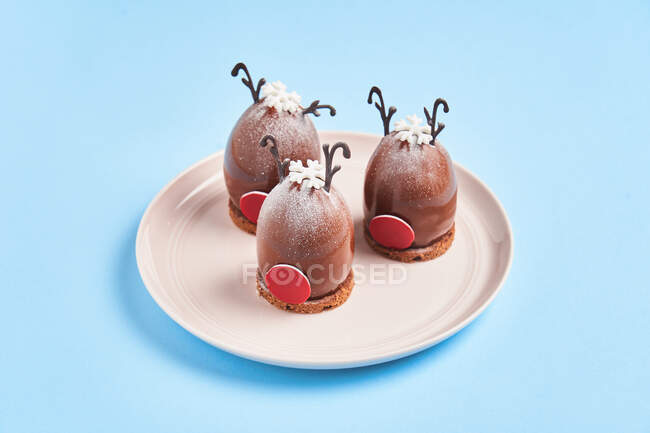From above deer head shaped desserts placed on plate on Christmas Day against blue background — Stock Photo
