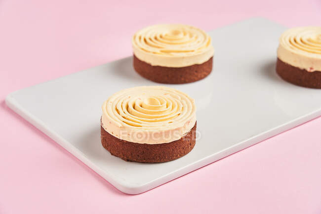 Крупним планом смачна шоколадна випічка, прикрашена вершковою спіраллю і розміщена на дошці на рожевому фоні — стокове фото