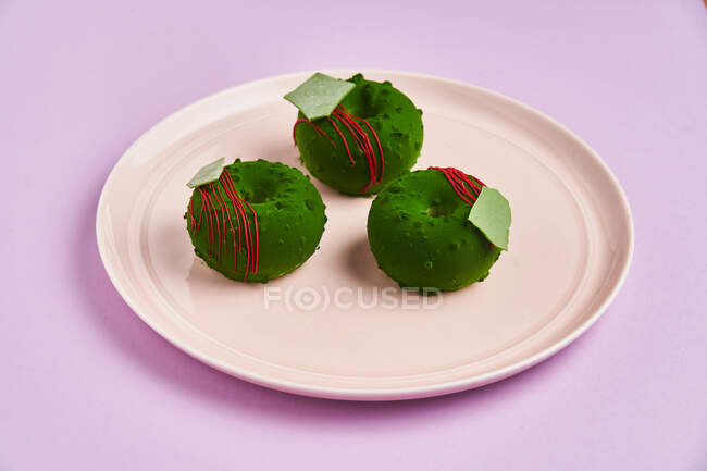De arriba sabrosos donuts frescos con glaseado verde colocado en el plato sobre fondo lila - foto de stock