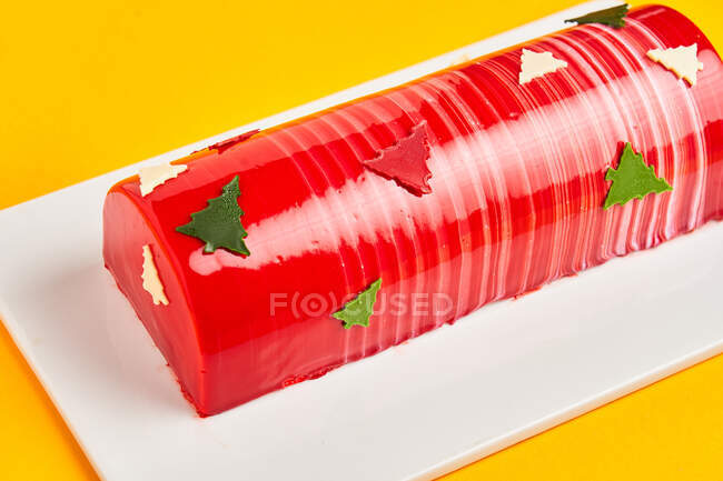 Зверху смачний торт з червоною глазур'ю та ялинками, розміщеними на дошці на жовтому тлі — стокове фото