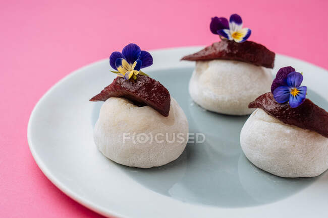 Випічка у формі каменю, прикрашена ягідним мармеладом та квітами і поміщена на тарілку на рожевому фоні — стокове фото