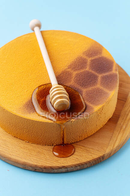 De arriba delicioso pastel de panal decorado con cuchara y miel líquida fresca sobre fondo azul - foto de stock