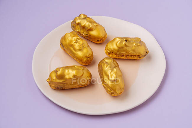 From above small fresh eclairs with golden icing placed on plate on lilac background — Stock Photo