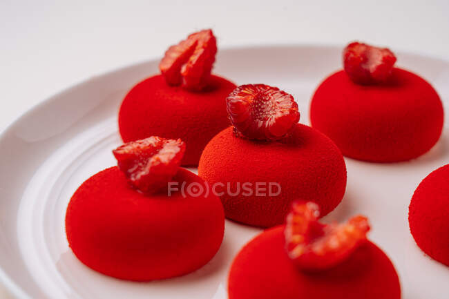 Closeup delectable cookies with vivid red icing and raspberries on top placed on white plate — Stock Photo