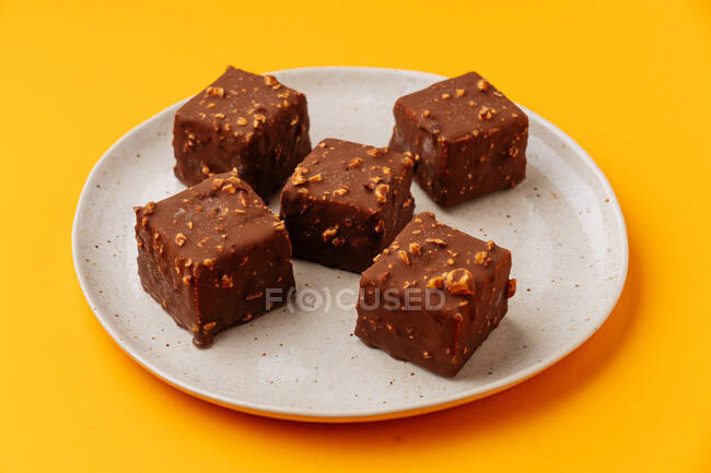 Dall'alto deliziosi biscotti cubici decorati con glassa al cioccolato e noci e disposti su piatto su sfondo giallo — Foto stock