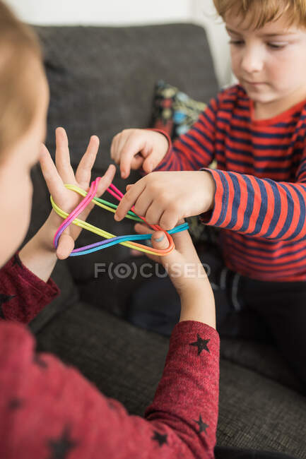 From above of little kids playing with colorful elastics on palms together at home — Stock Photo