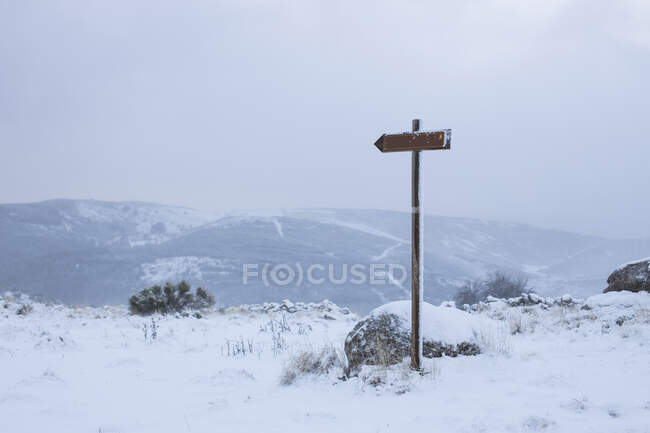 Small wooden guide sign on rocky roadside with mountainous terrain and blue cloudy sky on background — Stock Photo