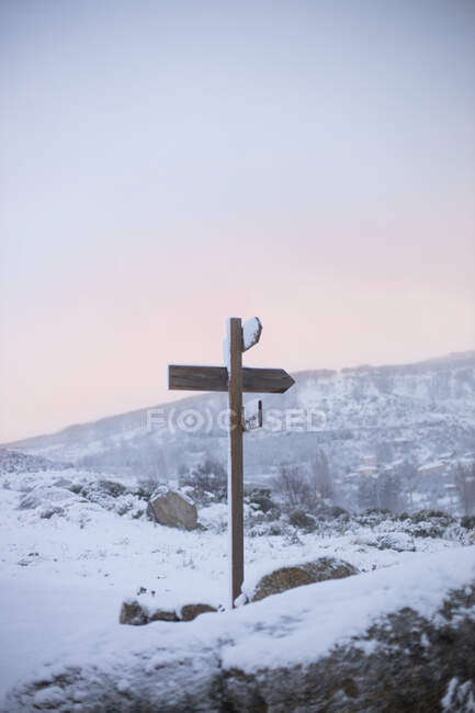Señal de flecha de madera en terreno solitario con montañas y cielo azul claro en el fondo - foto de stock