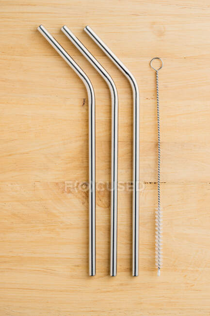 Top view of reusable metal straws and cleaning brush in row on wooden table — Stock Photo