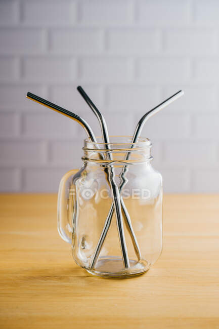Diverse cannucce di acciaio lucido in brocca di vetro vuota con manico su tavolo di legno — Foto stock
