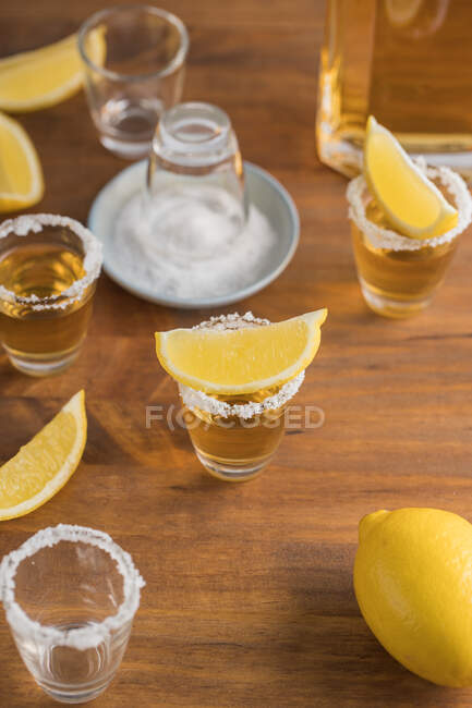 De cima vista superior de tiros de vidro de tequila dourada com borda salgada e fatias de limão em cima na mesa de madeira — Fotografia de Stock