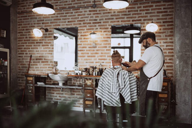 Back view of unrecognizable redhead man in modern hairdresser barber cutting his hair — Stock Photo
