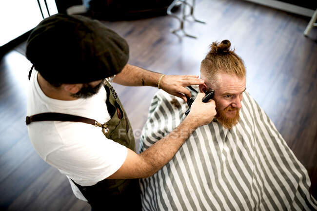 Von oben schneidet der moderne Friseur einem erwachsenen Mann im Friseurstuhl die Haare — Stockfoto