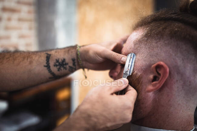 Pessoas de culturas irreconhecíveis no moderno cabeleireiro barbeiro cortando um cabelo ruivo em cadeira de barbeiro — Fotografia de Stock