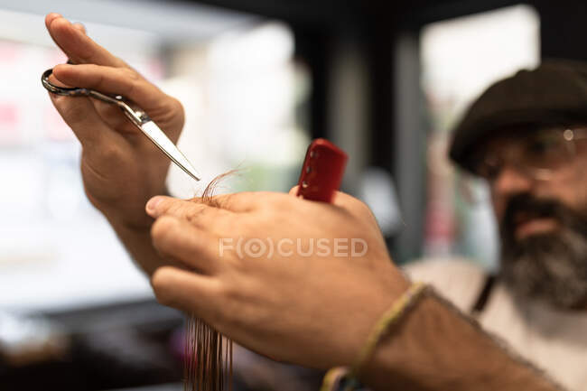 Unrecognizable blurred man hairdresser holding scissors and comb cutting costumer hair in modern barbershop — Stock Photo