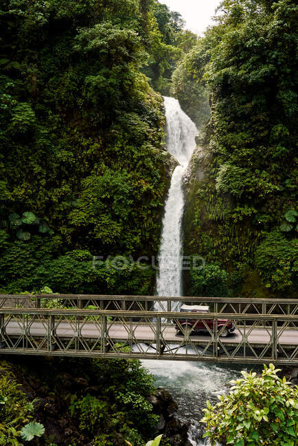 Véhicule vintage chevauchant le long d'un pont près d'une cascade incroyable dans la jungle du Costa Rica — Photo de stock