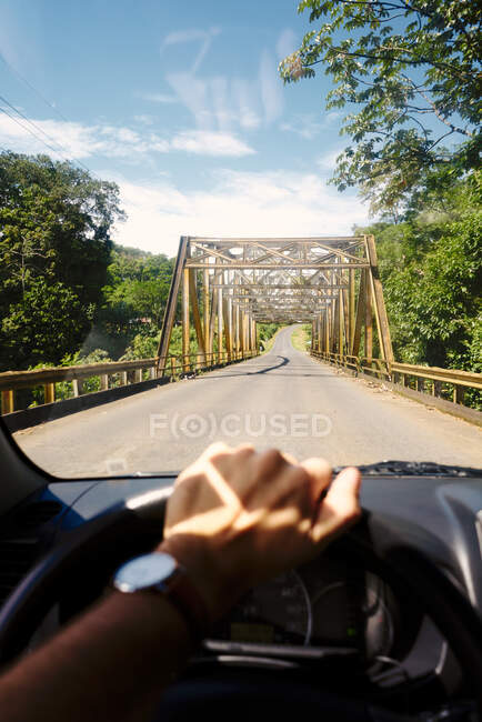 Unrecognizable person steering vehicle on asphalt road towards modern bridge on sunny day in Costa Rica — Stock Photo